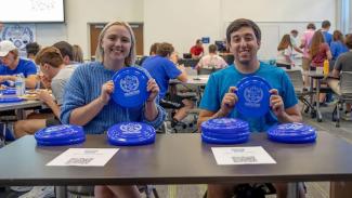 Two students hold frisbees while tabling at an event.