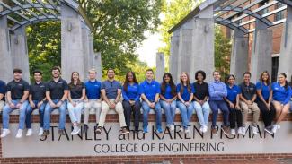 Ambassadors and peer mentors sit on the College of Engineering sign.